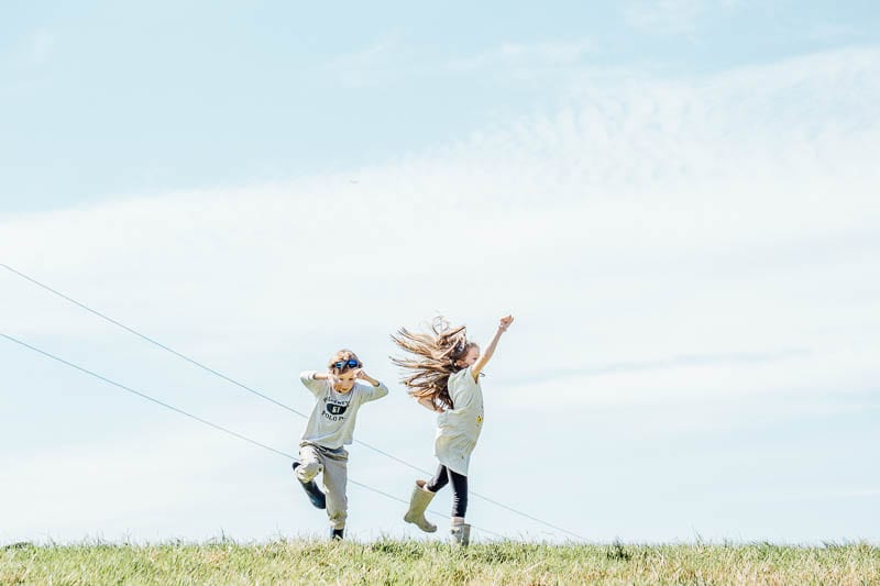 Twins in August leaping in field against blue sky